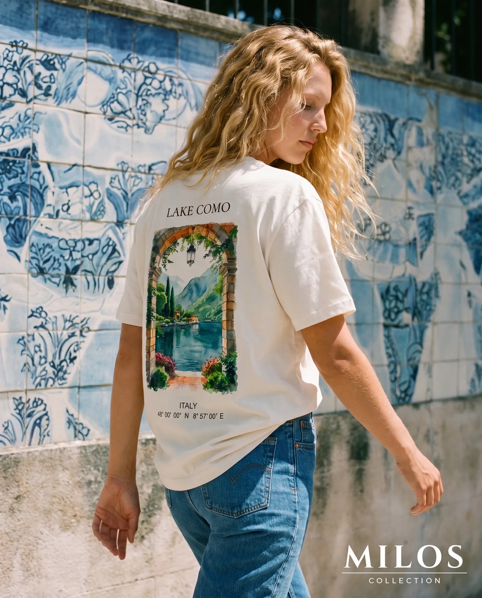 Femme de dos portant le t-shirt Lake Como, devant un mur d'azulejos bleus et blancs.